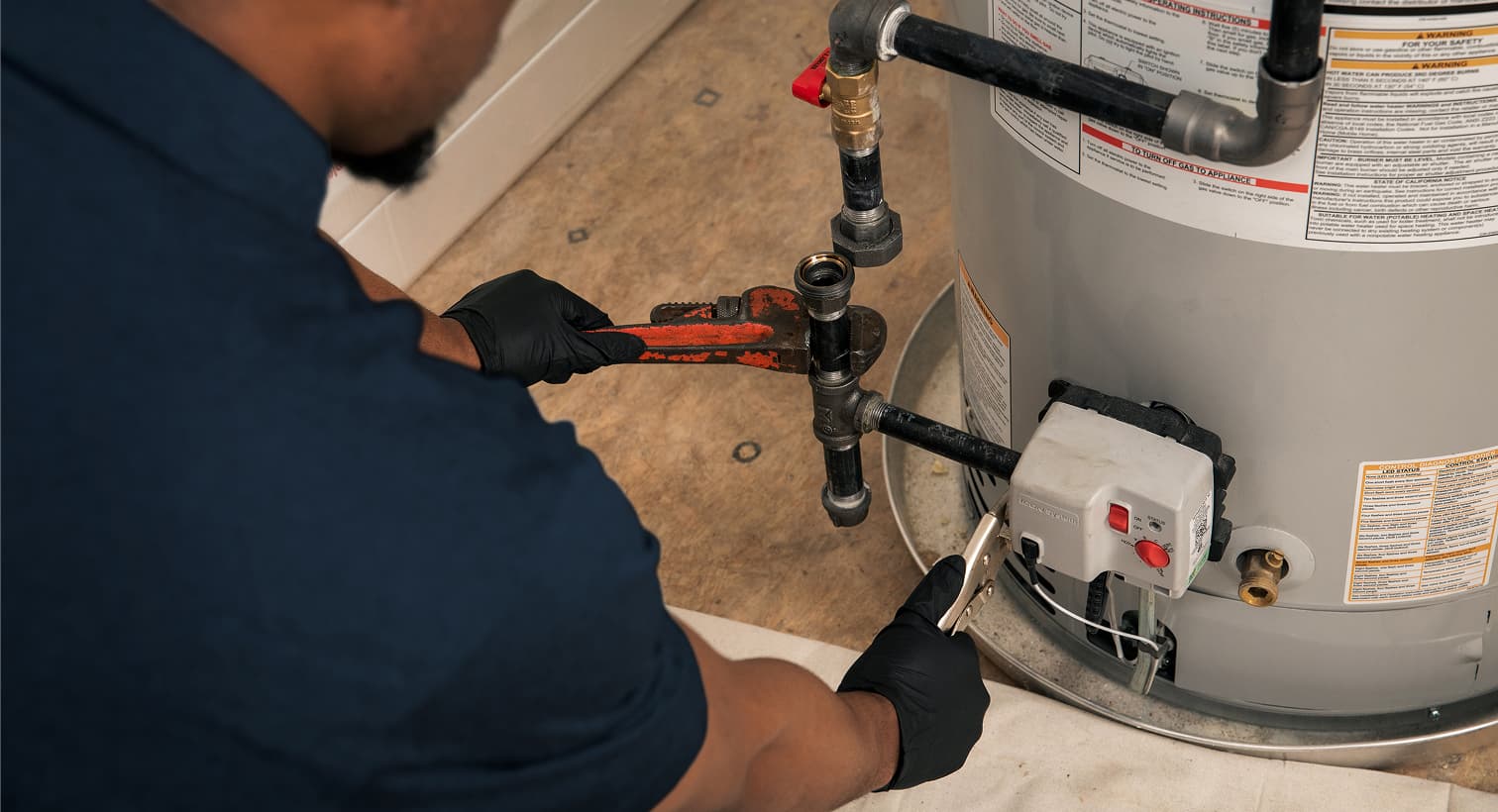 A professional Hutchinson plumber using a pipe wrench to fix a residential water heater during a home plumbing repair service.