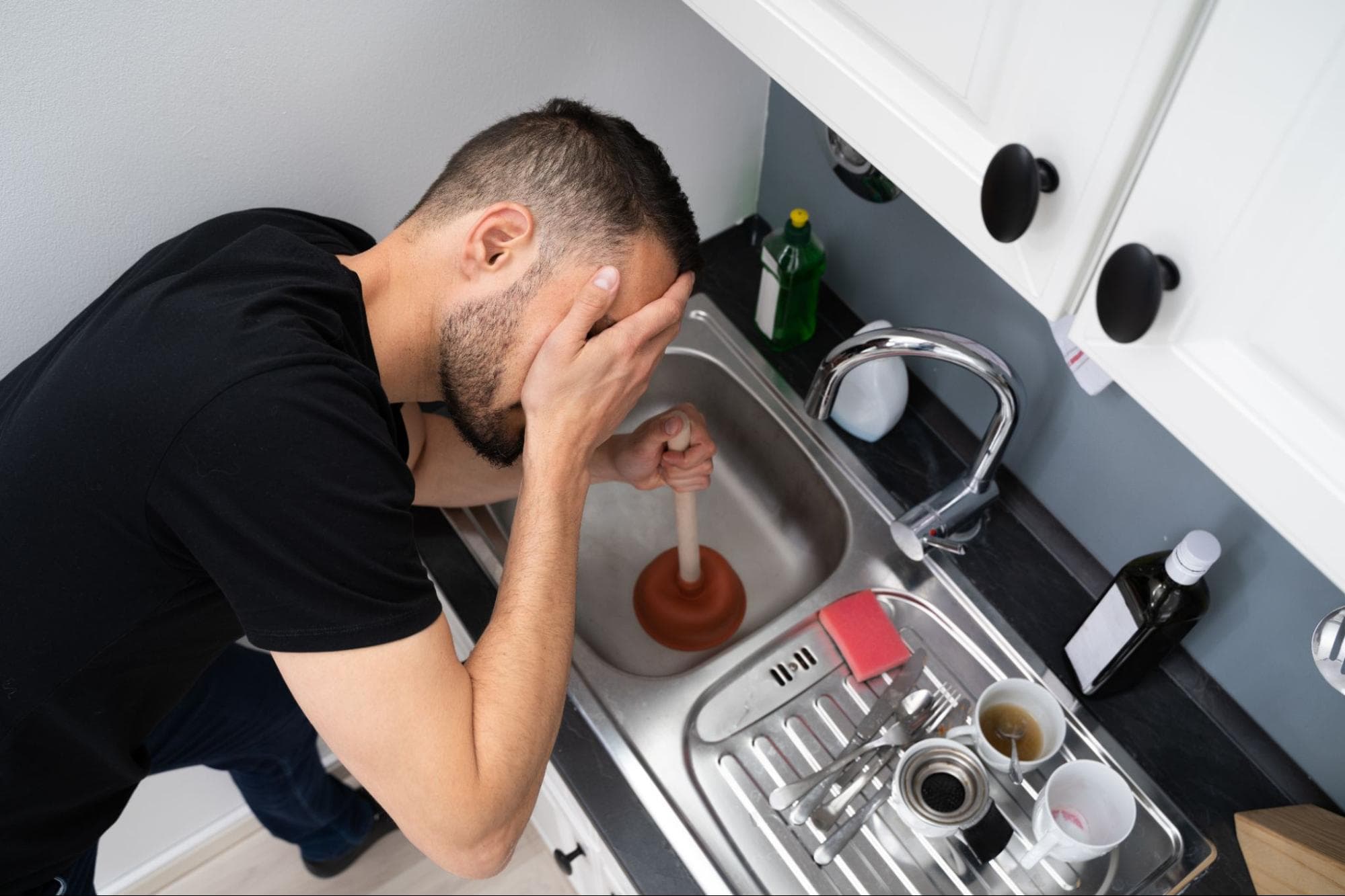 homeowner struggling using a plunger in kitchen sink