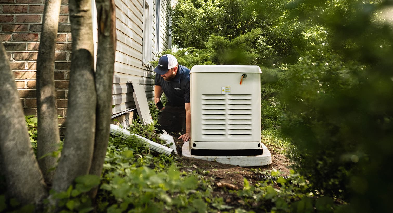 A professional Hutchinson technician inspects a large, beige whole-home standby generator installed on a concrete pad outside a residential house.