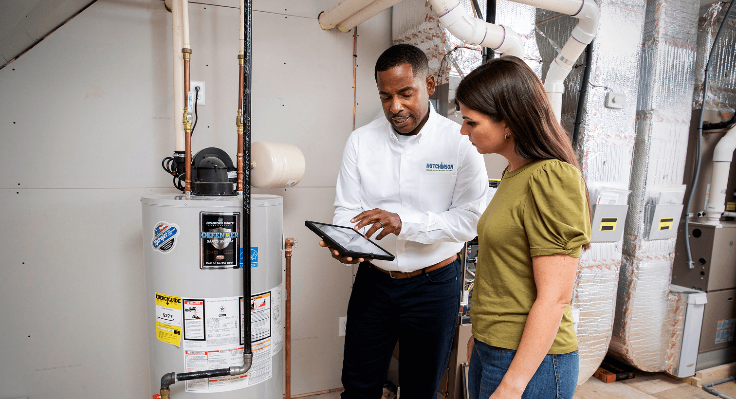 Plumbing technician reviewing inspection results with a homeowner near a residential water heater.