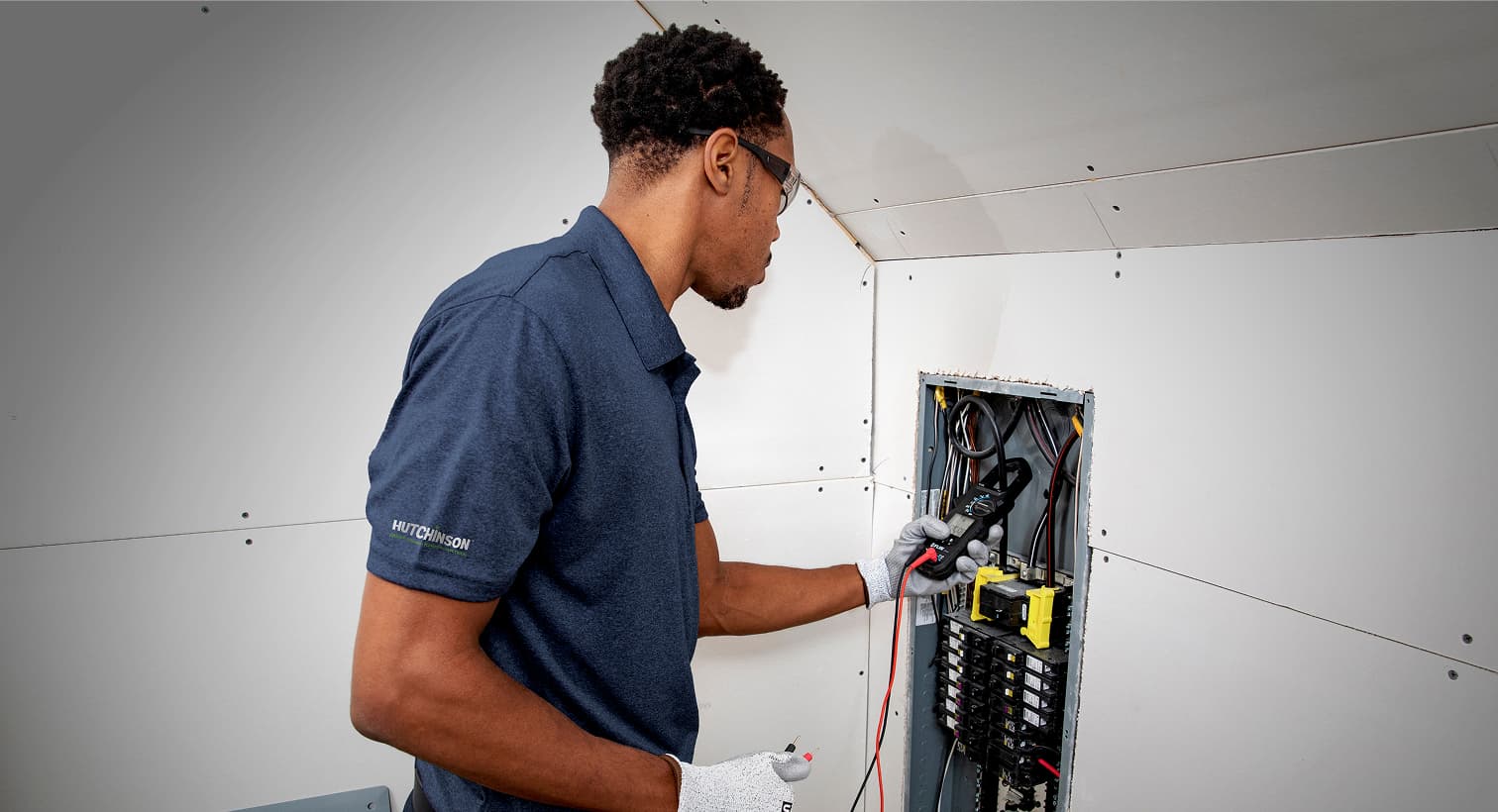 A professional Hutchinson electrician using a digital multimeter tool to test and inspect a residential electrical panel during a circuit breaker service call.