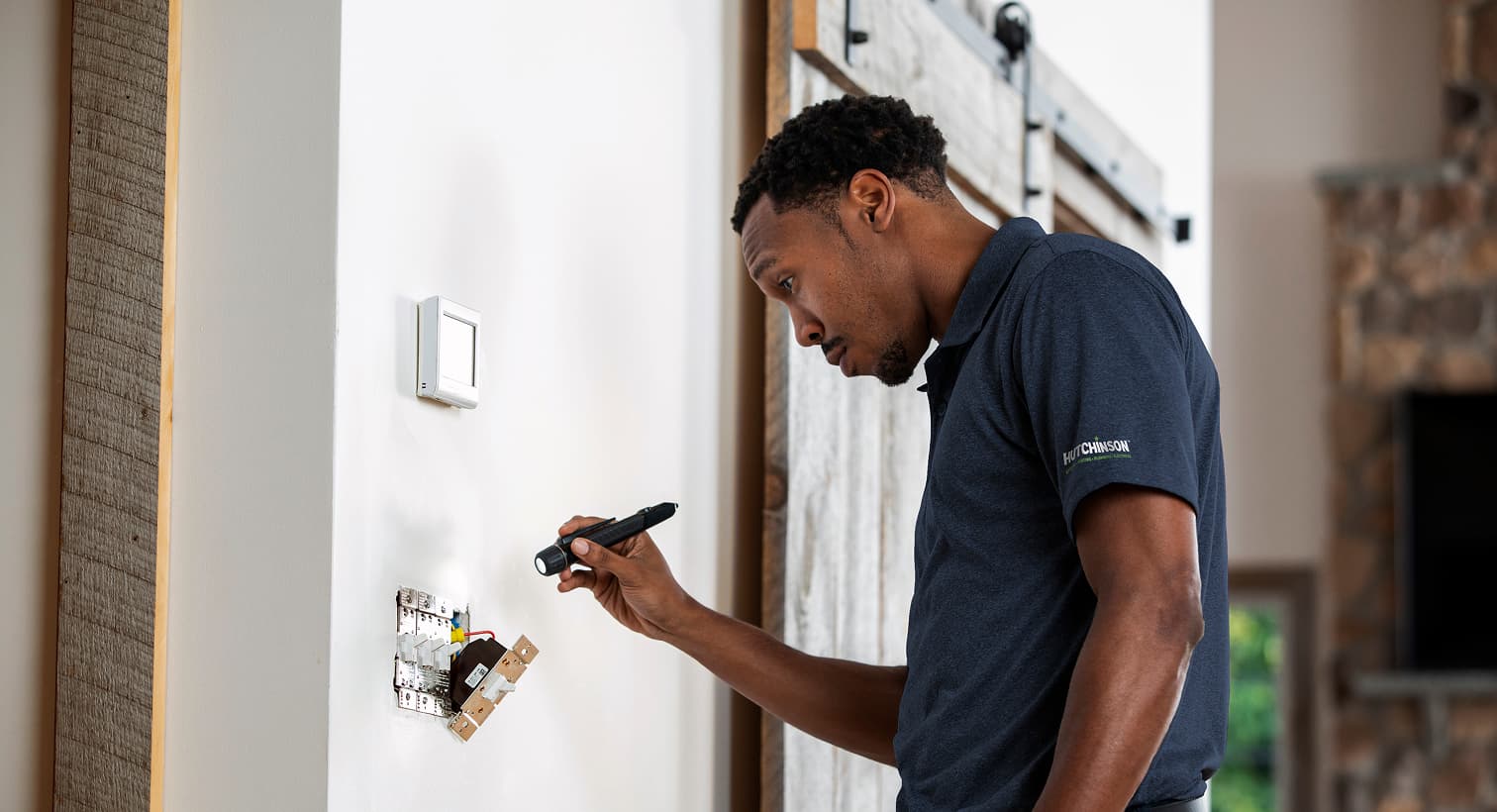 A professional Hutchinson electrician using a flashlight to safely inspect and troubleshoot exposed residential wall switch wiring during an electrical repair service.
