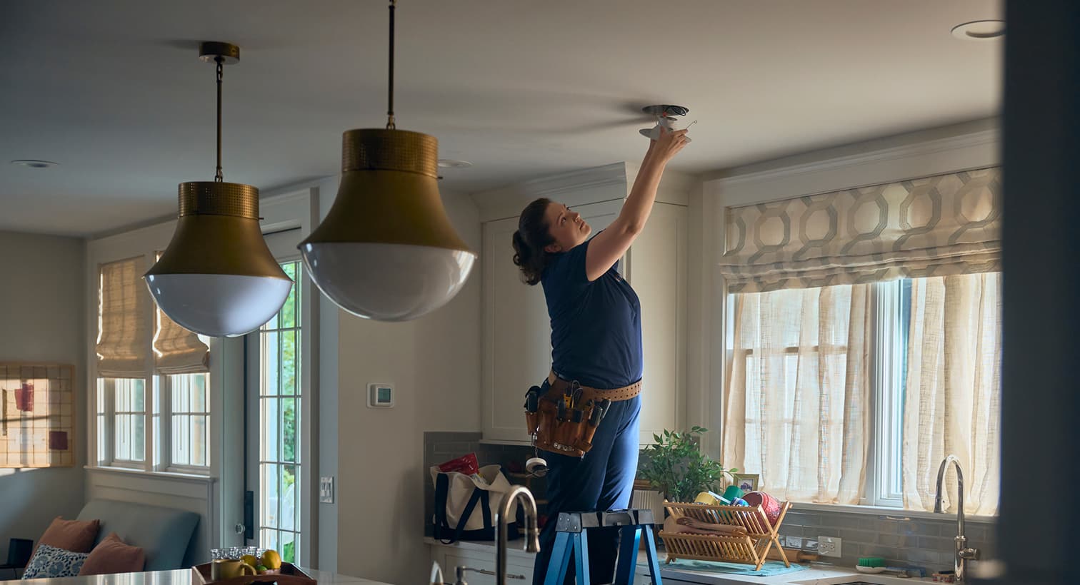 A professional Hutchinson electrician standing on a ladder to install modern recessed ceiling lights during a residential electrical installation service.