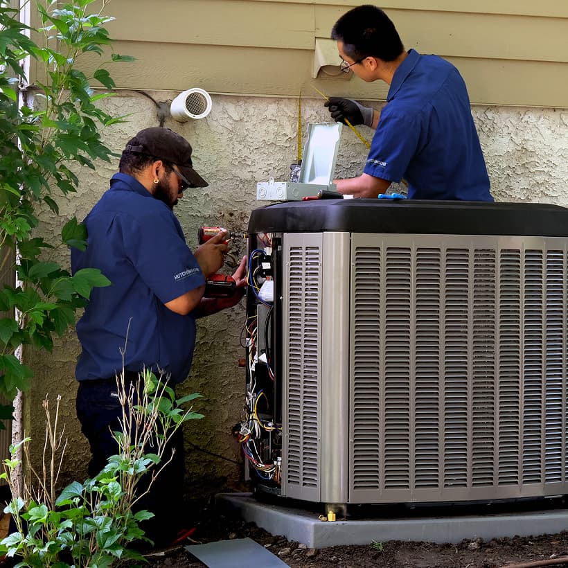 Two Hutchinson HVAC technicians installing a brand-new residential outdoor air conditioning condenser unit during a home AC replacement service.